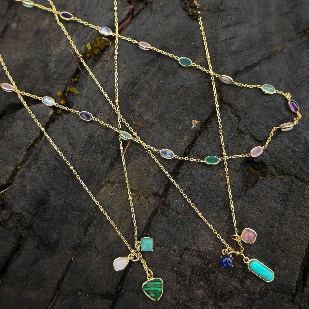 Gold necklaces with colorful gemstones on a dark stone surface