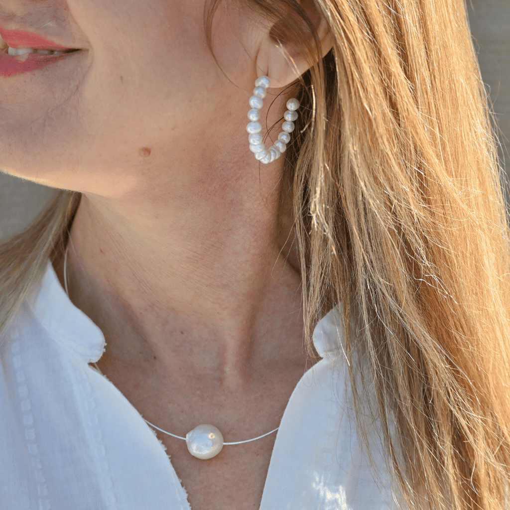 Close-up of a woman wearing pearl hoop earrings and a necklace with a blurred background