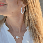 Close-up of a woman wearing pearl hoop earrings and a necklace with a blurred background
