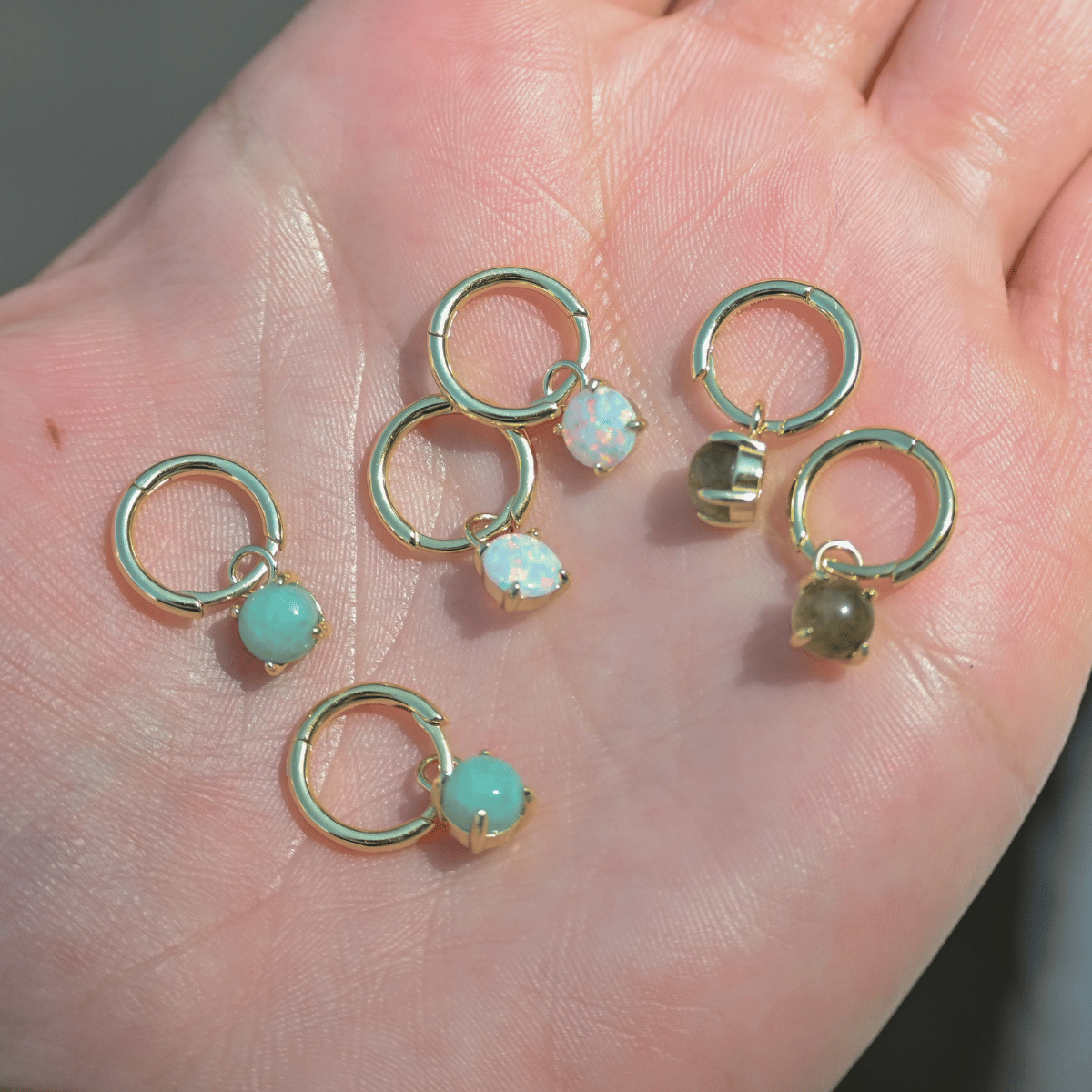 Gold hoop earrings with gemstones on a hand