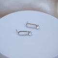 Pair of silver earrings with clear gemstones on a white surface