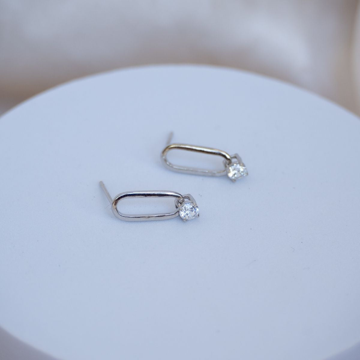 Pair of silver earrings with clear gemstones on a white surface