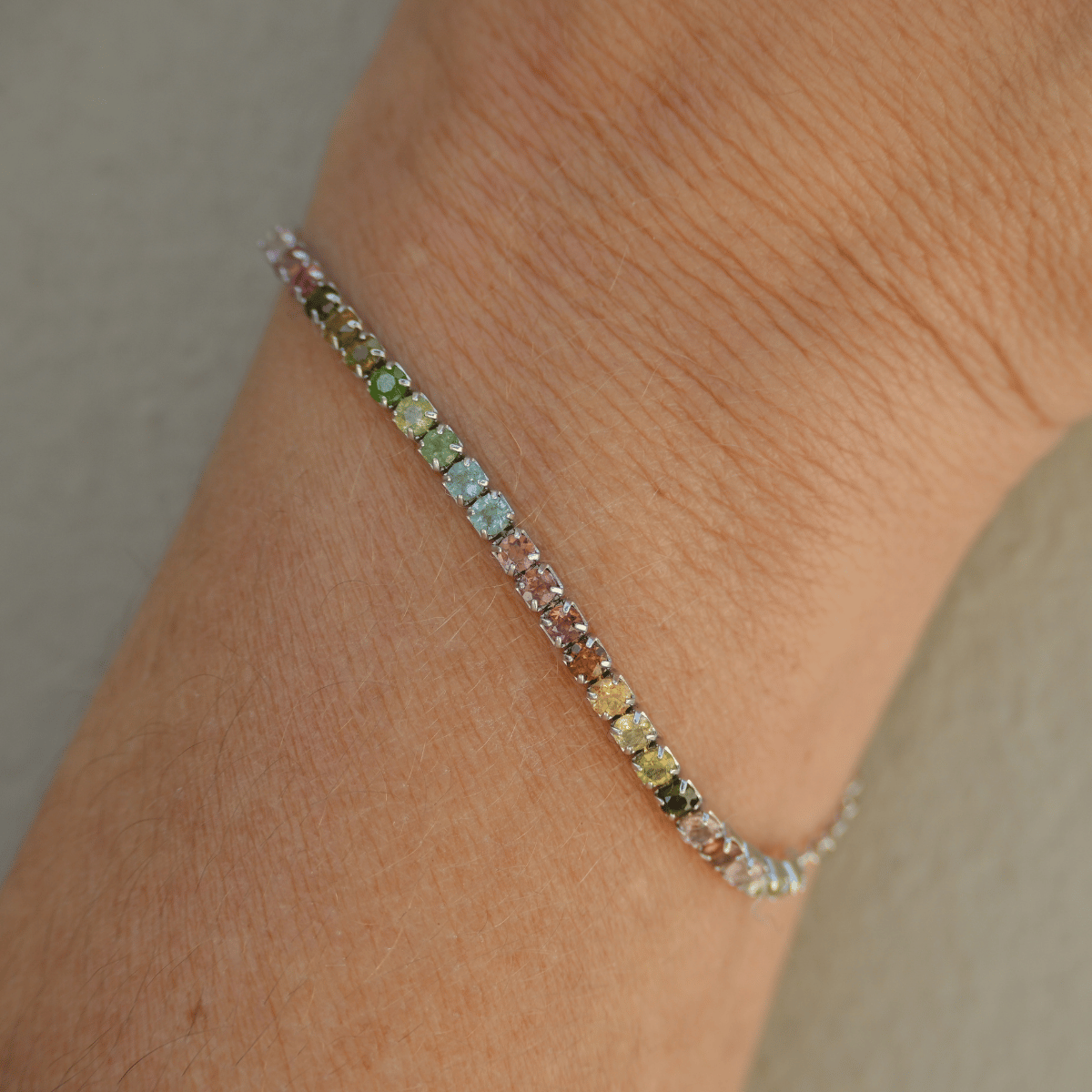 Multicolored gemstone bracelet on a wrist against a neutral background