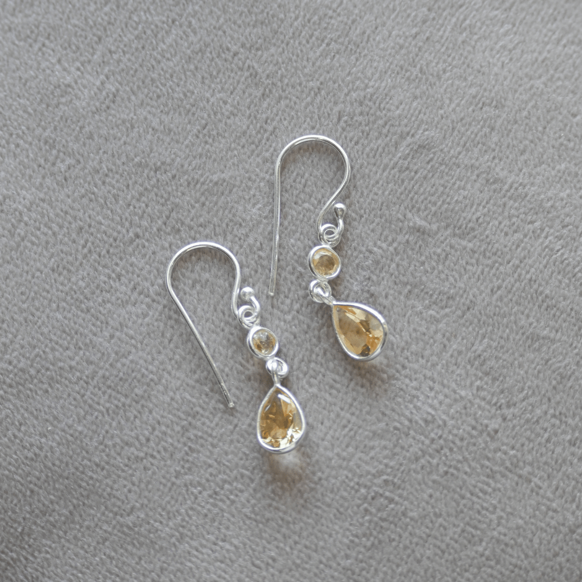 Silver earrings with teardrop-shaped yellow gemstones on a gray background
