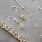 Jewelry set with silver chain necklace, bracelet, and earrings on a gray background