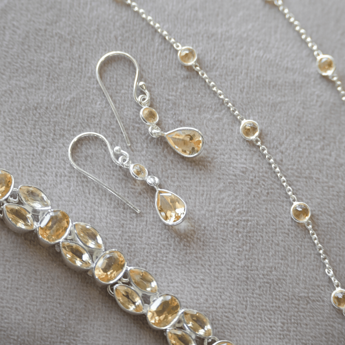 Jewelry set with silver chain necklace, bracelet, and earrings on a gray background