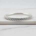 A sterling silver hollow bracelet with a geometric spiral pattern, displayed on a white surface next to a green plant.