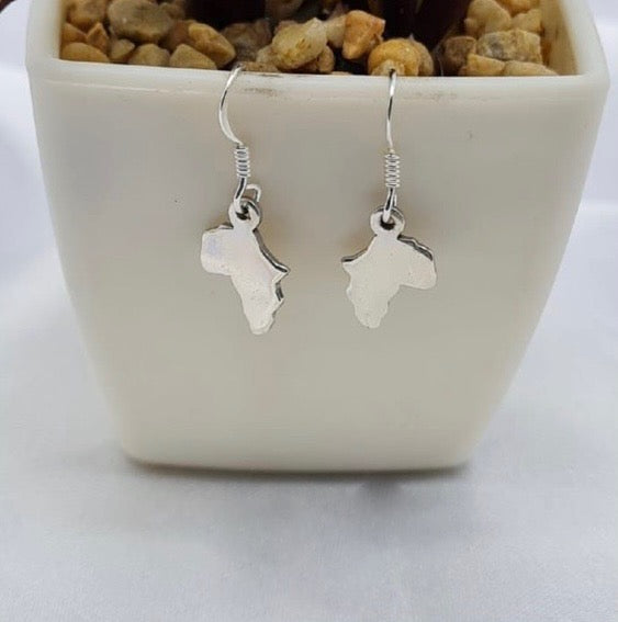 A pair of sterling silver drop earrings designed in the shape of Africa, displayed in a white vase with a textured background.