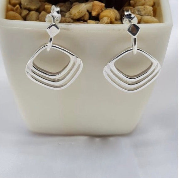 A pair of sterling silver drop earrings displayed in a white vase, with a rock-like pattern on the top of each earring.
