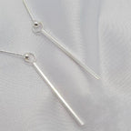 A pair of sterling silver bar drop earrings displayed on a white fabric surface.